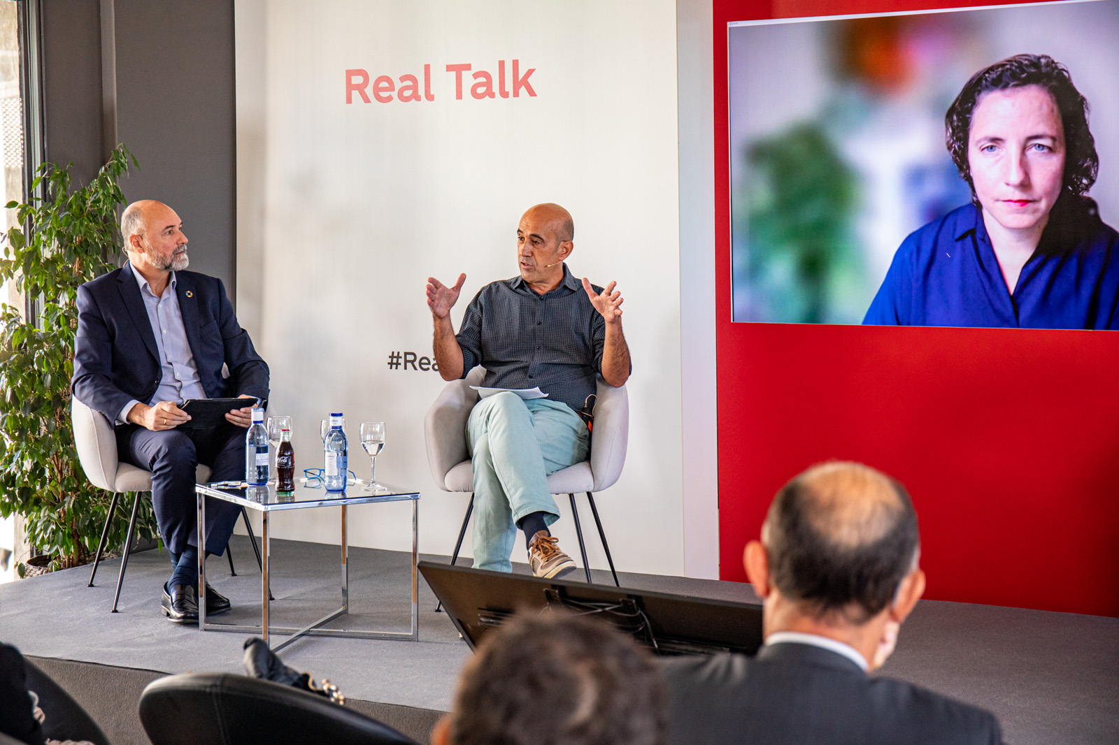 Dos hombres hablando en un escenario con público