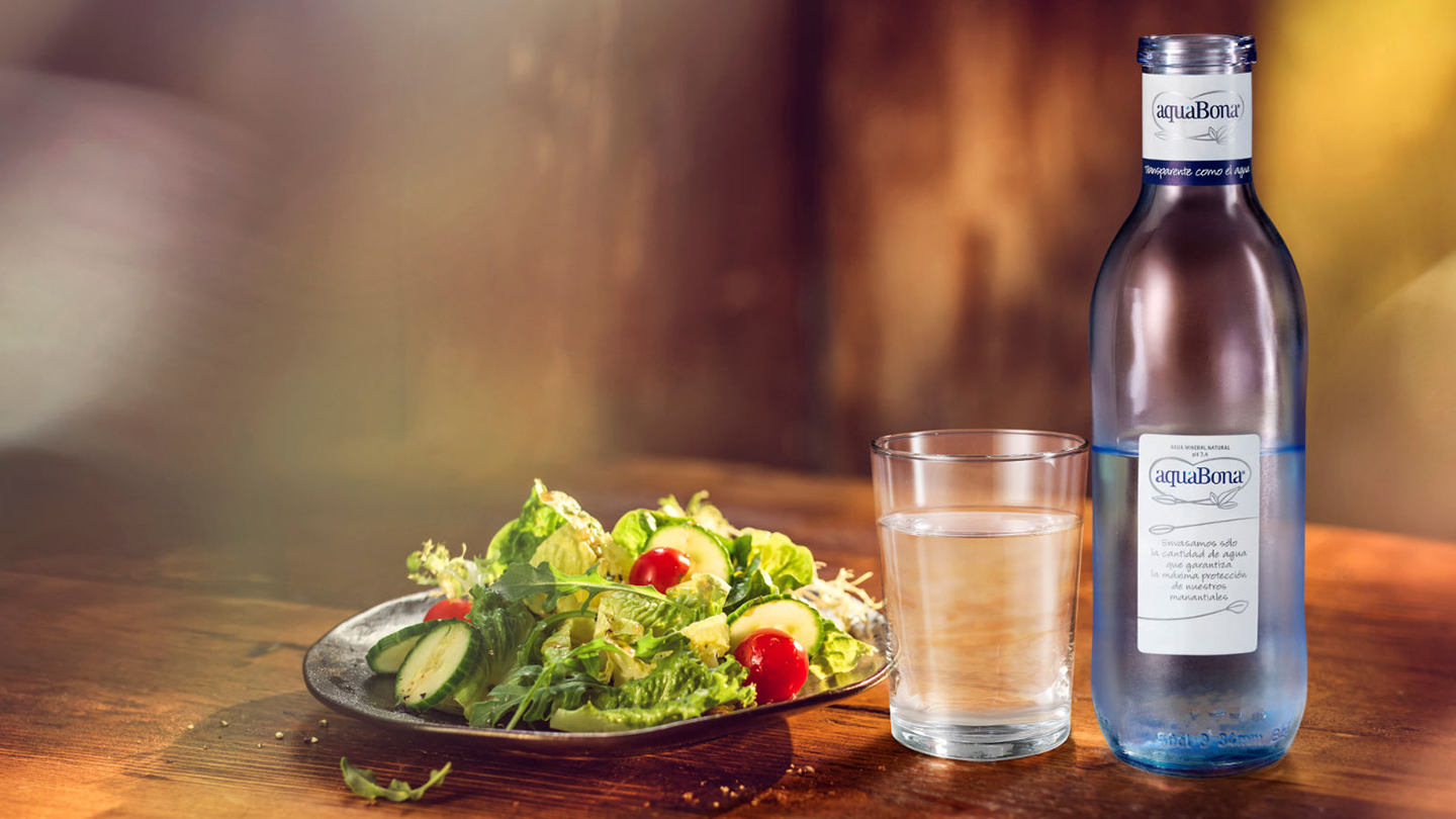 Botella de aquaBona junto a vaso y plato de comida sobre una mesa