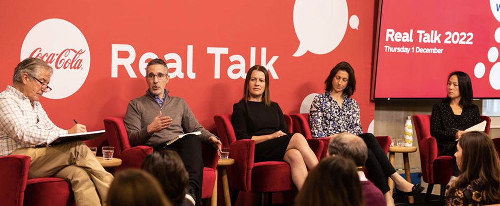 Five people sitting and talking in front of a panel that says Coca-Cola Real Talk