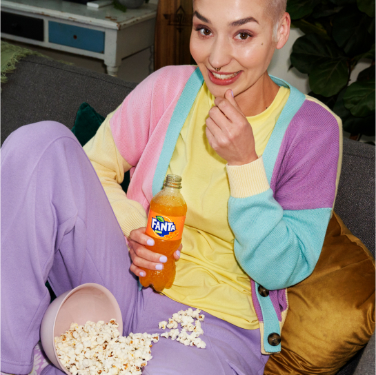 En kvinna i färgglada kläder med en Fanta Orange Zero Sugar