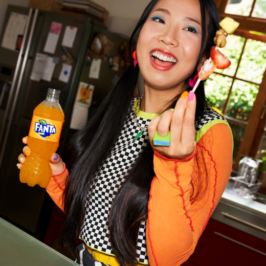 Woman with bottle of Fanta and fruit on cocktail stick