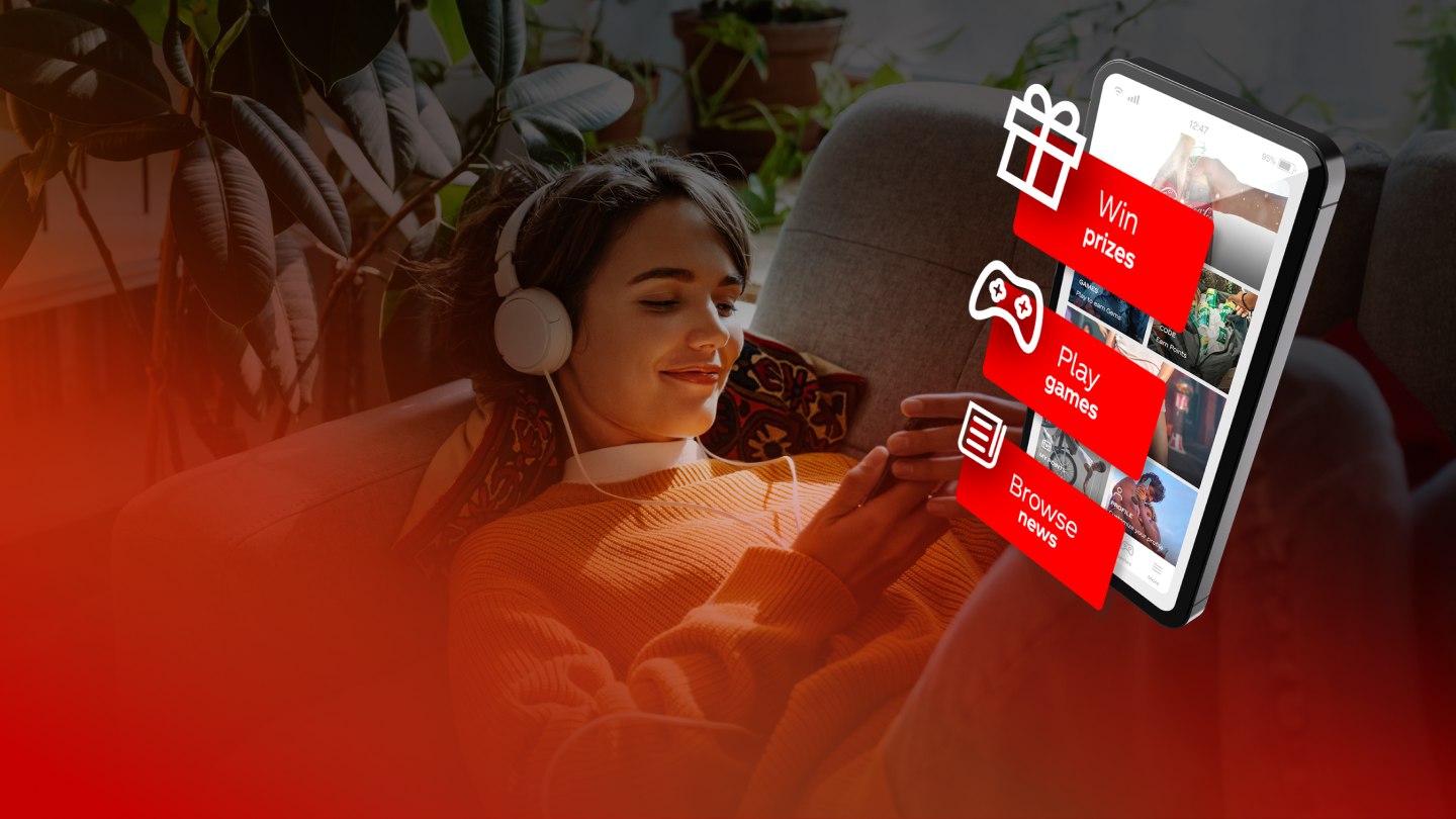 Une personne est allongée confortablement sur un canapé et regarde un smartphone affichant une interface rouge Coca‑Cola tout en tenant une boisson. Au premier plan, une lueur rouge floue est visible.