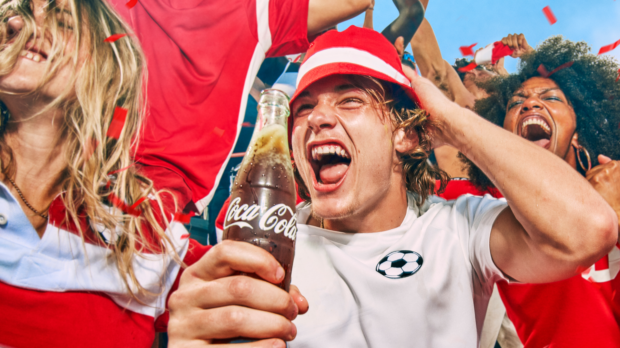 Фен гледа футбол и се радва. Държи стъклена бутилка с Coca-Cola