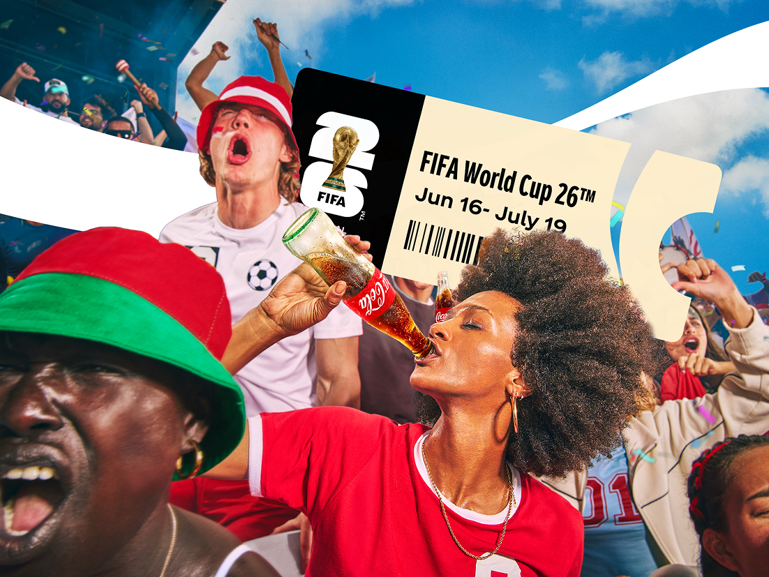 Supporters en tenue de football célèbrent avec énergie en levant les bras et en chantant. Une personne boit dans une bouteille rouge Coca‑Cola, tandis que des drapeaux et un ciel bleu en arrière‑plan renforcent l’ambiance festive et sportive.