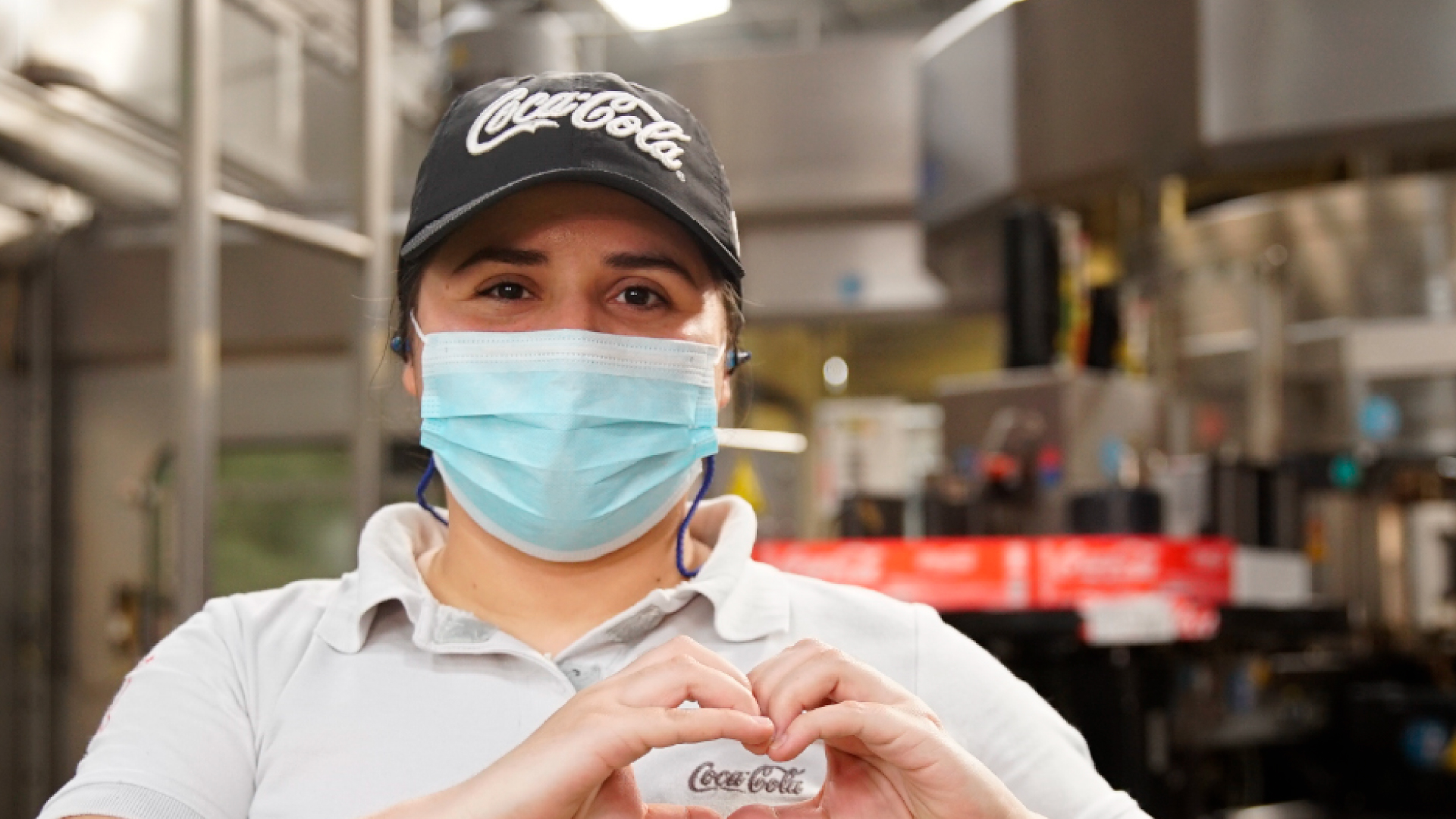Mujer mirando a cámara sonriente con una gorra de Coca-Cola y una mascarilla.
