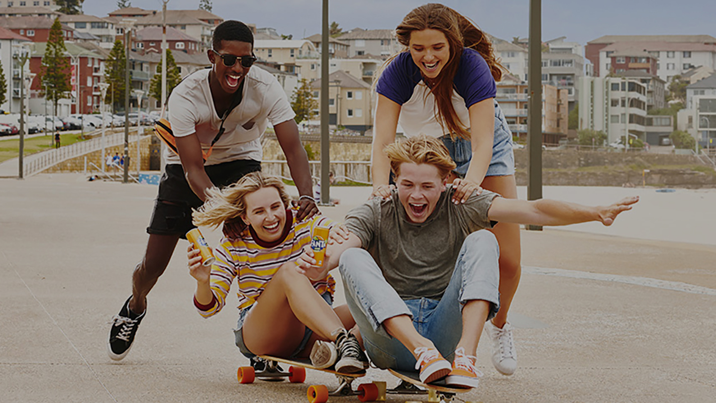 一群年青人在人行道上玩滑板，他們手裏拿着芬達汽水罐