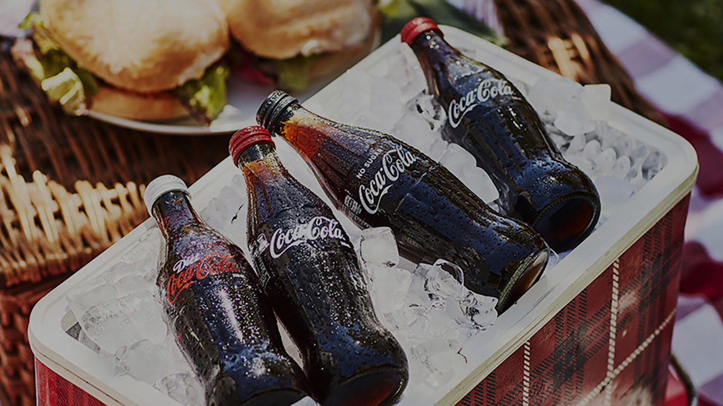 Cooler with ice full of Coca-Cola bottles in a picnic scenario