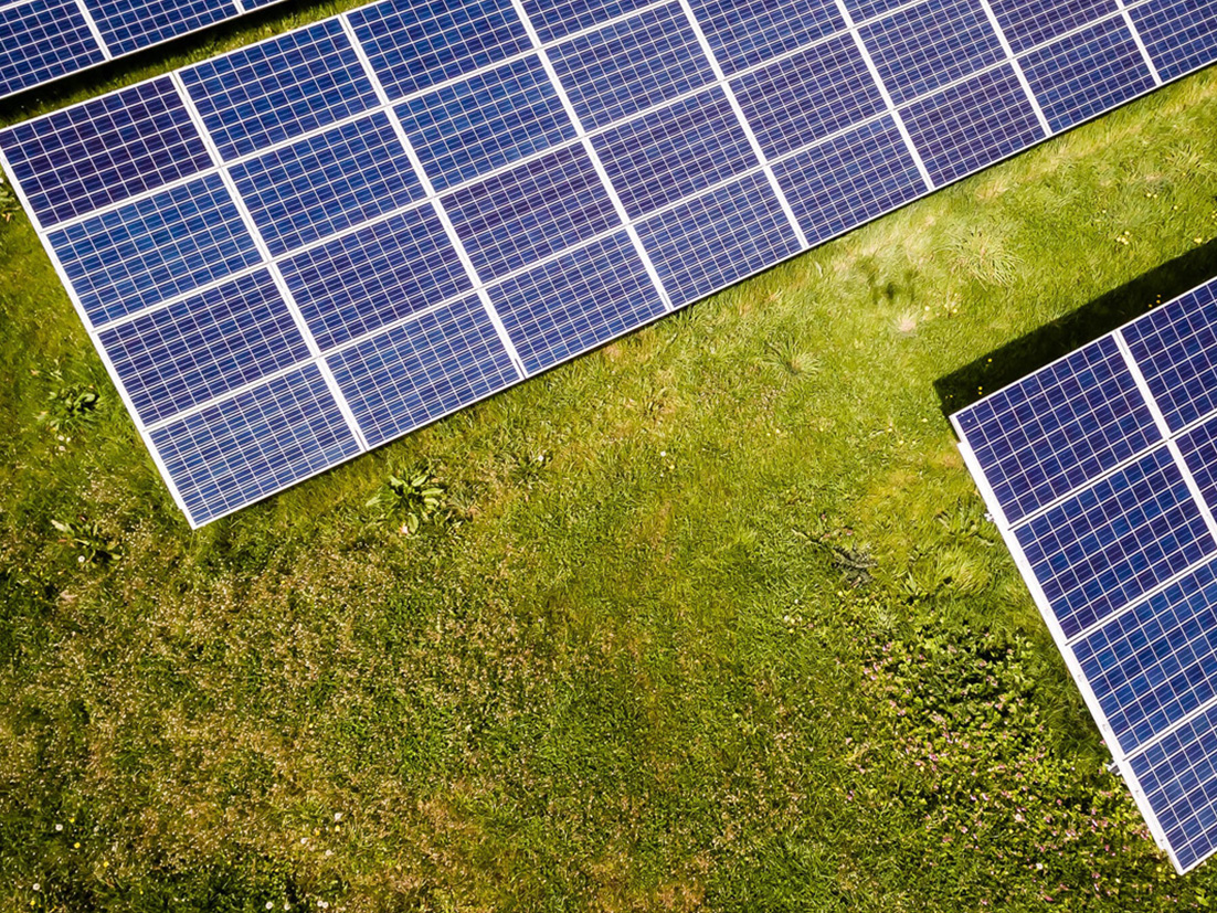 從上方俯視一片綠色田野上的太陽能電池板/一片農田的開放視野，前景有兩人正在行走。