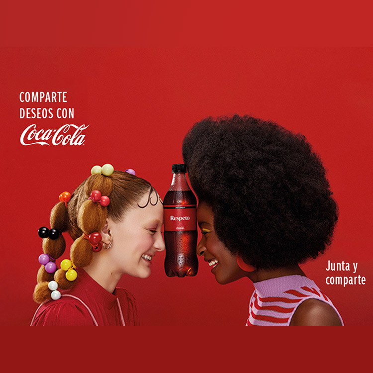 Dos mujeres sostienen juguetonamente una botella de Coca-Cola entre sus frentes.