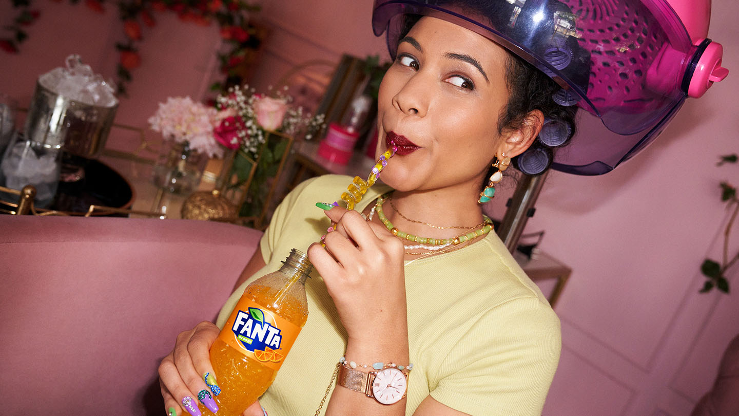 Žena sprema frizuru dok kroz spiralnu slamku pije Fanta naranču iz boce