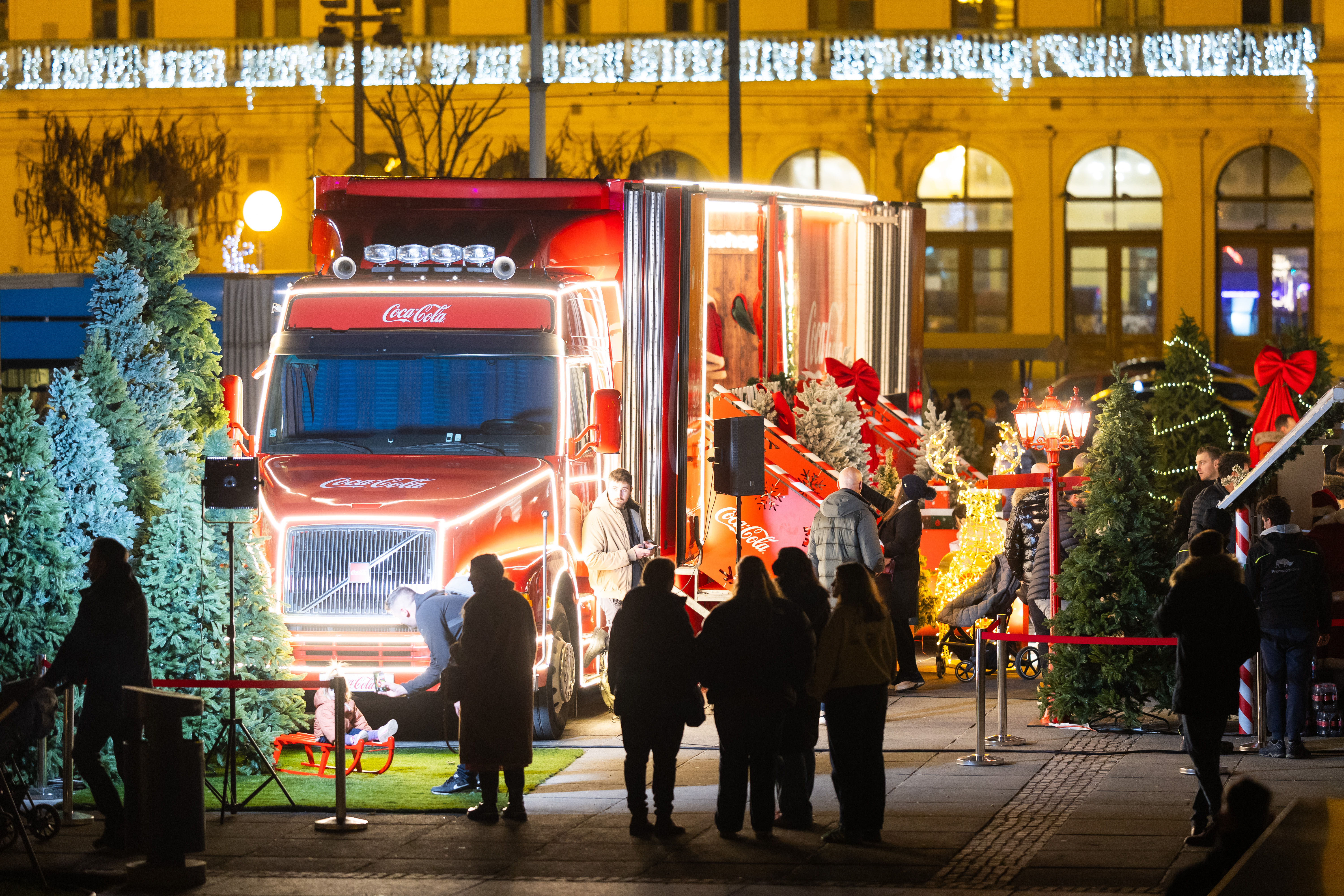 Coca‑Colin božićni kamion osvijetljen blagdanskim dekoracijama na Adventu u Zagrebu, okružen posjetiteljima i u sklopu humanitarne akcije