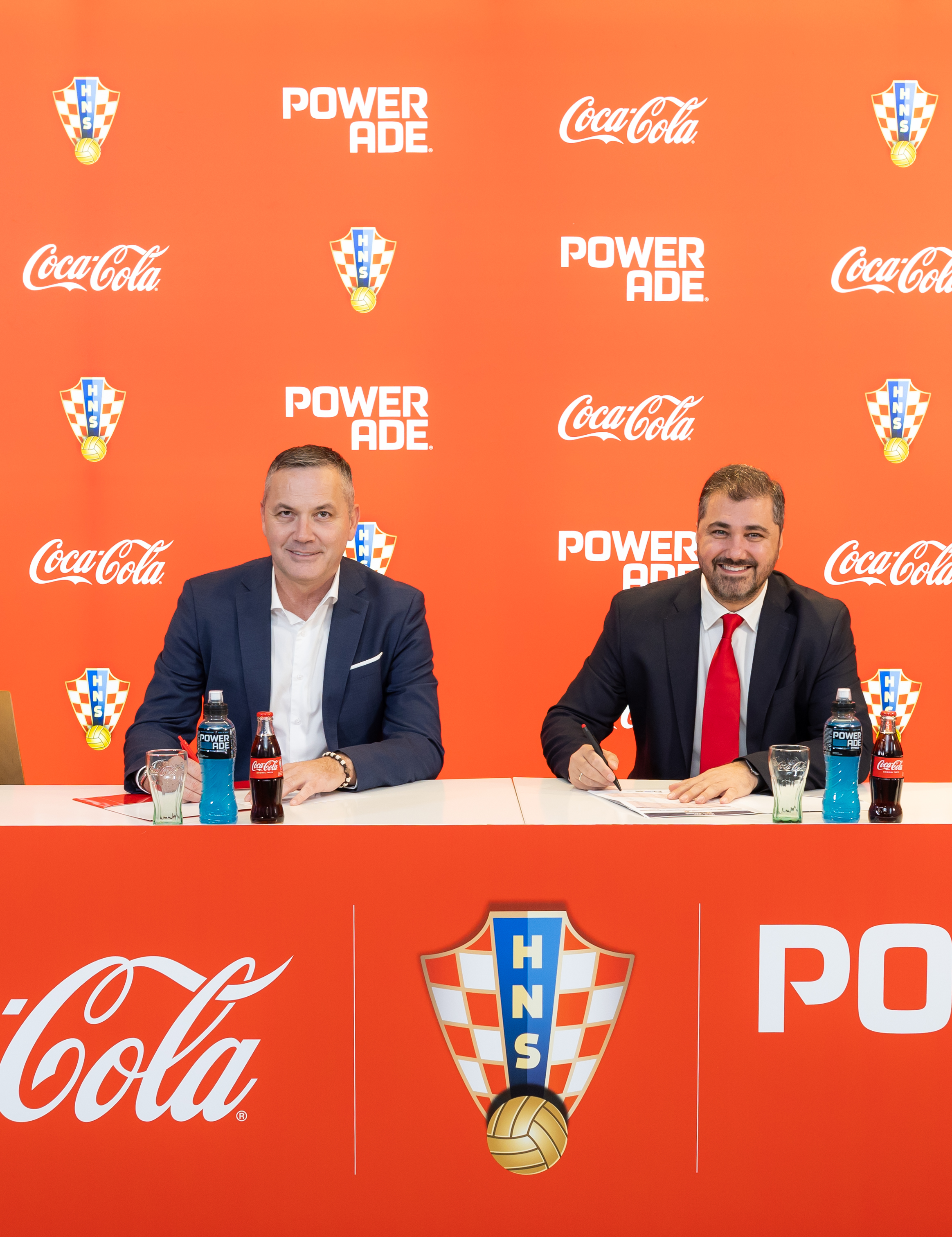 Potpisivanje sponzorskog ugovora između Hrvatskog nogometnog saveza i Coca‑Cole, uz izložene proizvode Coca‑Cole i Powerade ispred brendirane pozadine.