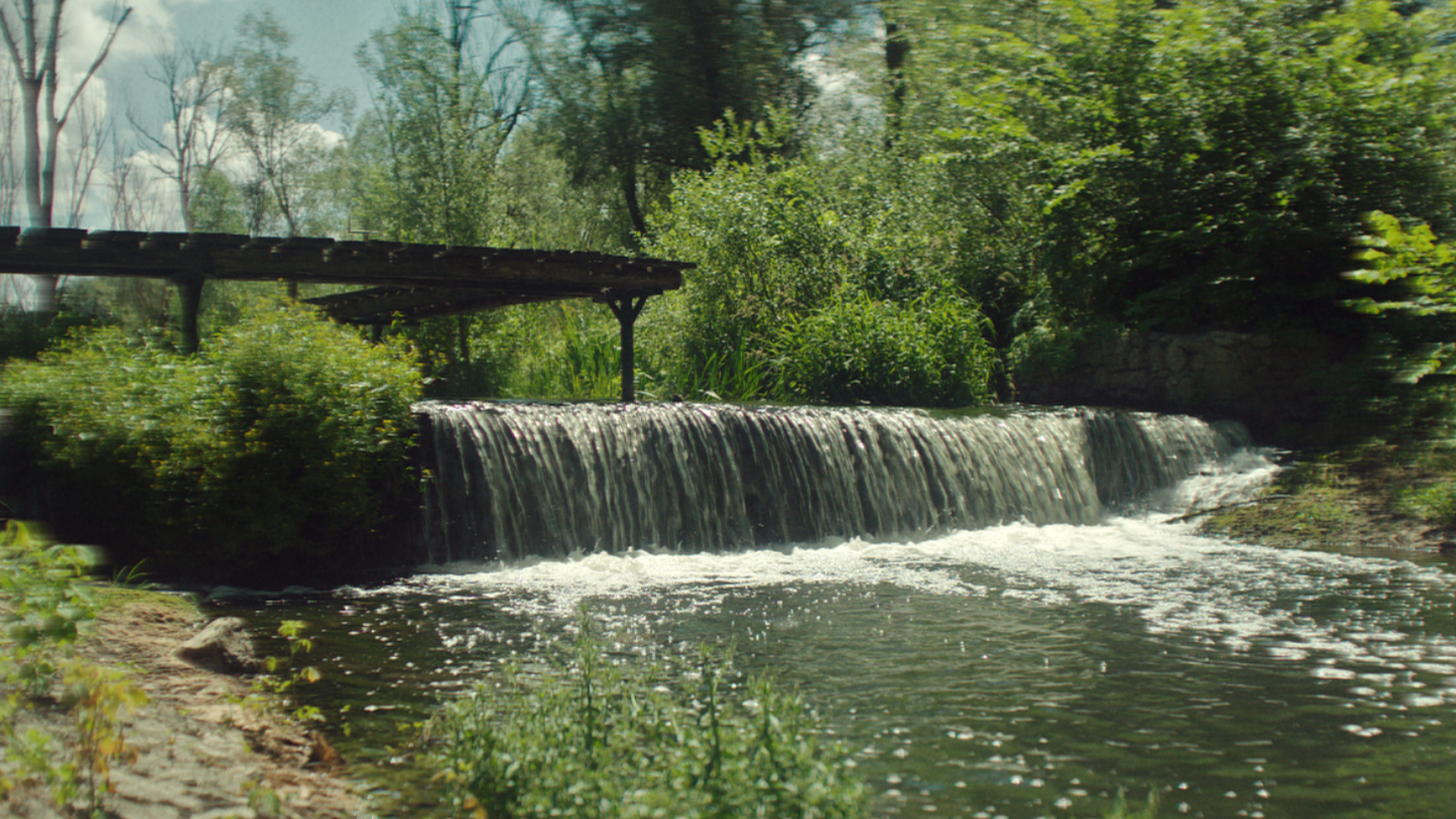 Mali slap koji se prelijeva preko drvene brane okružen zelenilom i bujnom vegetacijom.