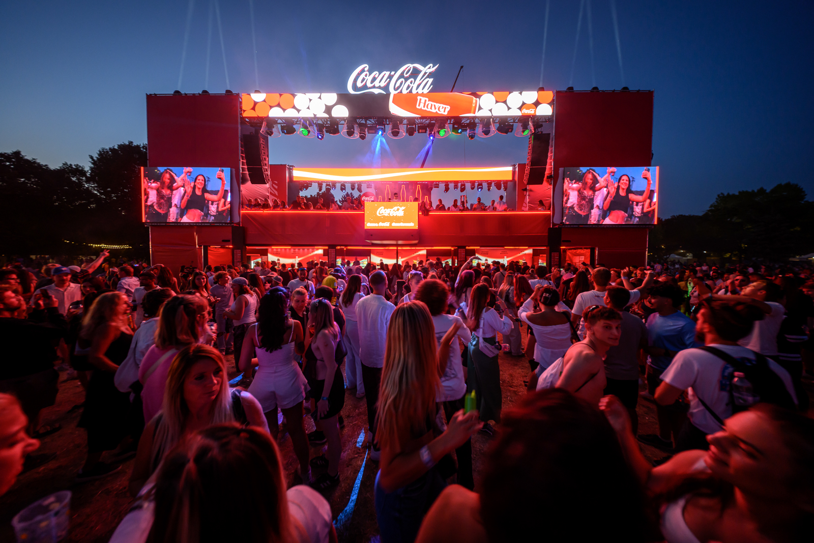 Koncerthelyiség nagy tömeggel és Coca-Cola felirattal a színpadon