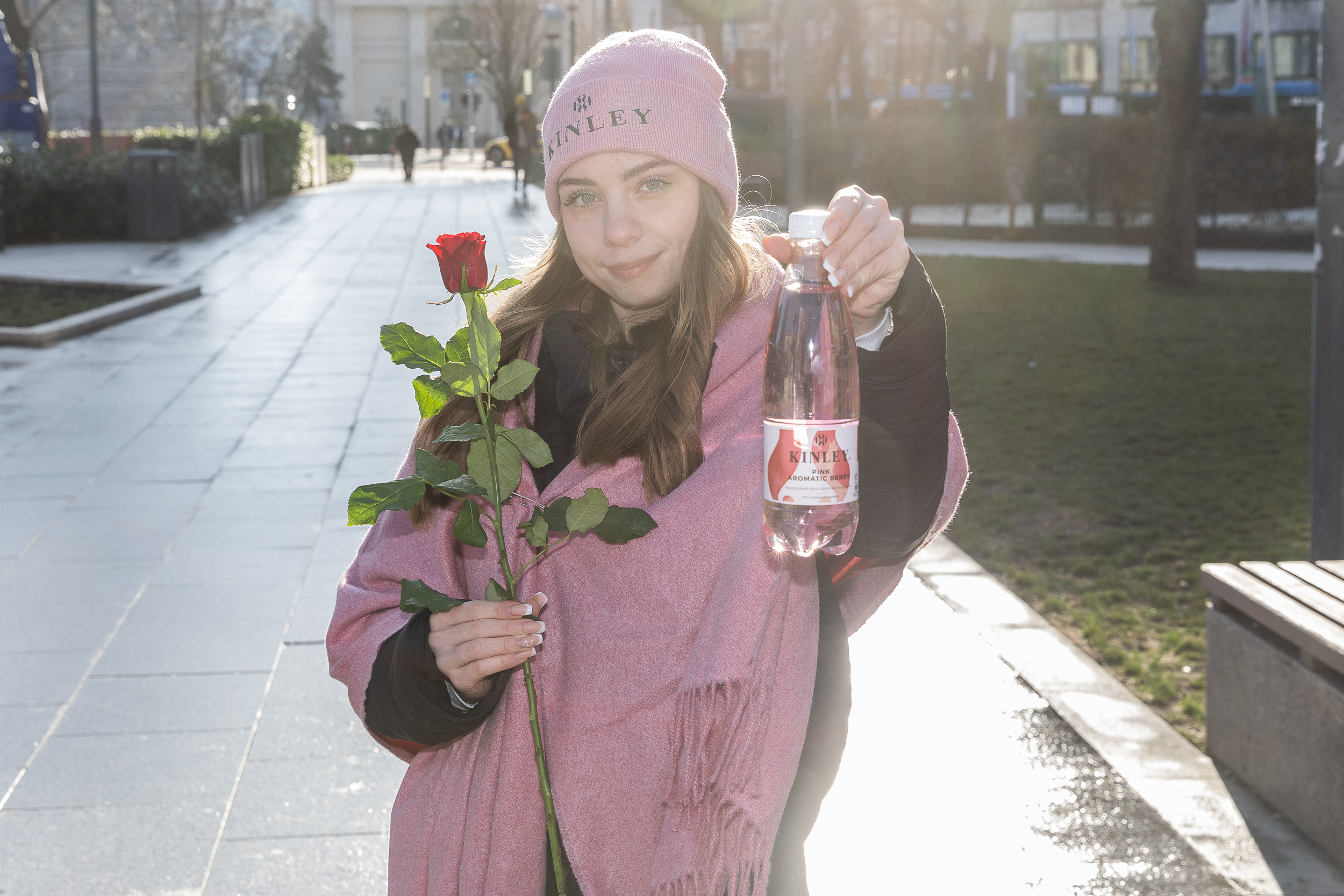 Egy kalapos lány, aki Kinley üveget és rózsát tart a kezében