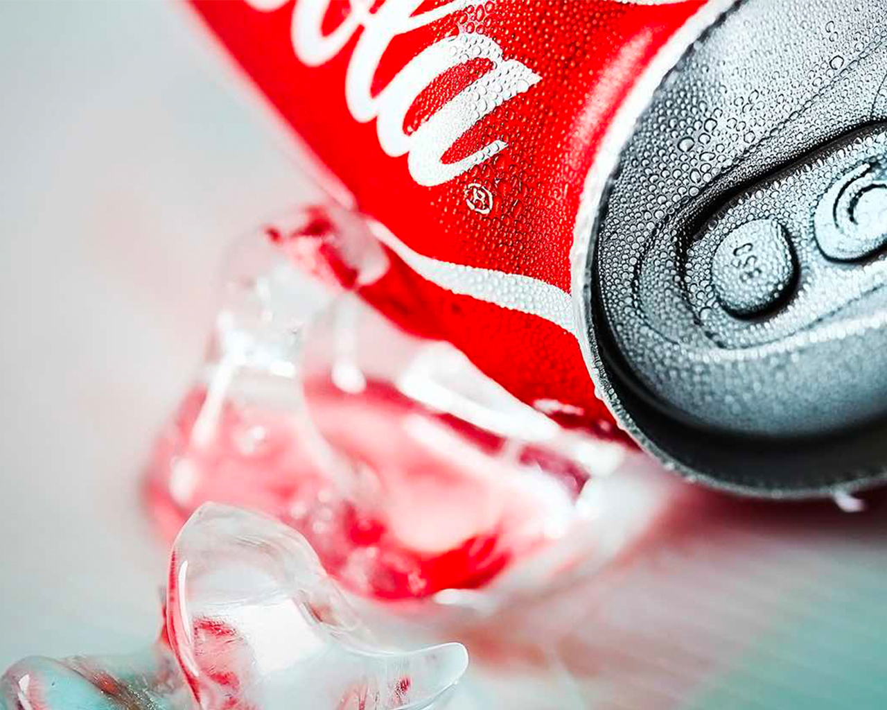 A Coca-Cola can laying next to cubes of ice on a white surface