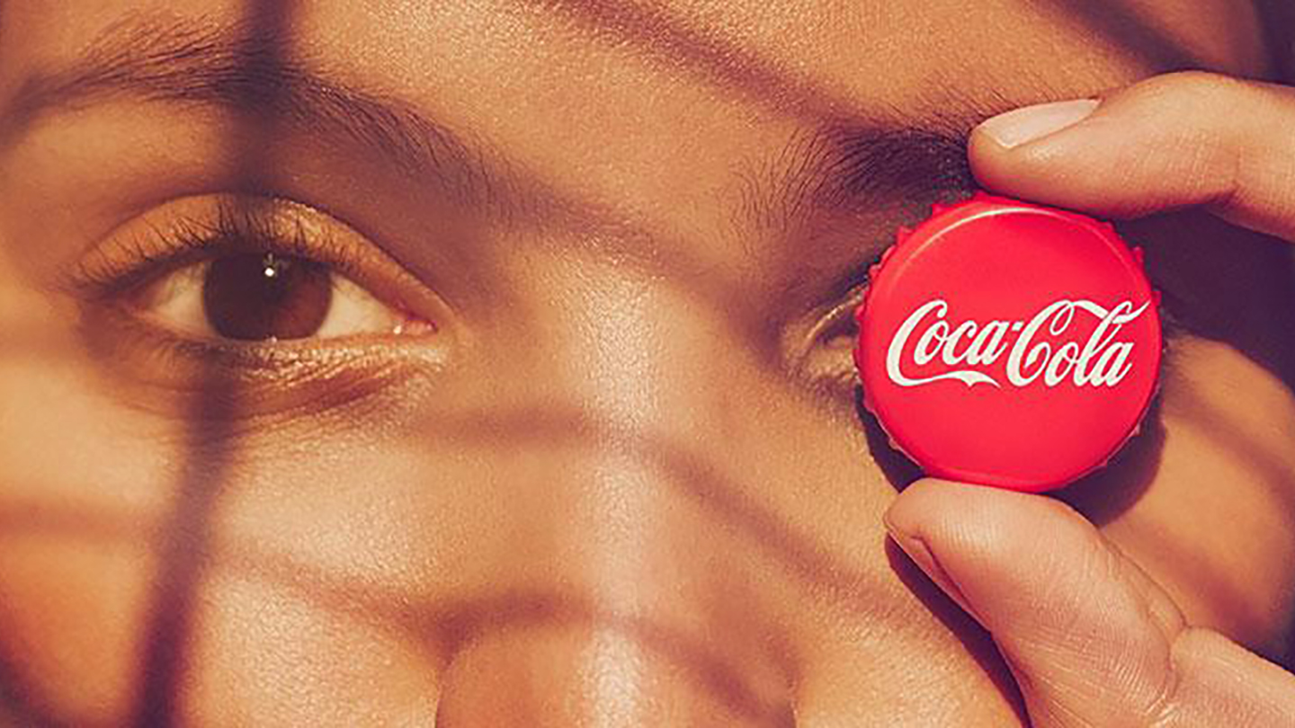 A woman holding a Coca-Cola cap in front of her left eye