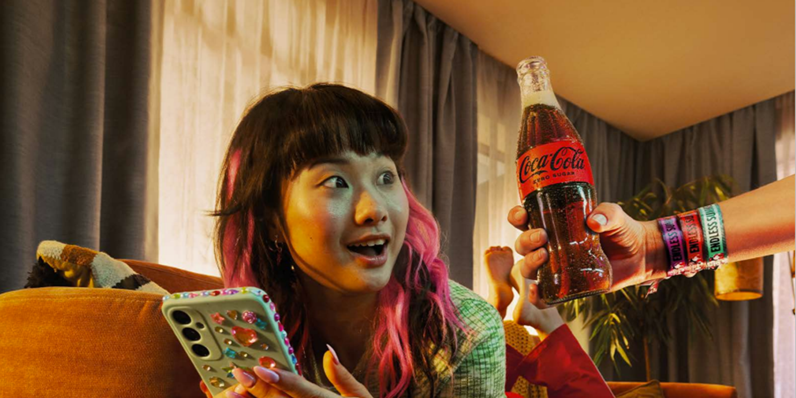 teenager scrolling on her phone looking at a glass bottle of coca-cola zero sugar