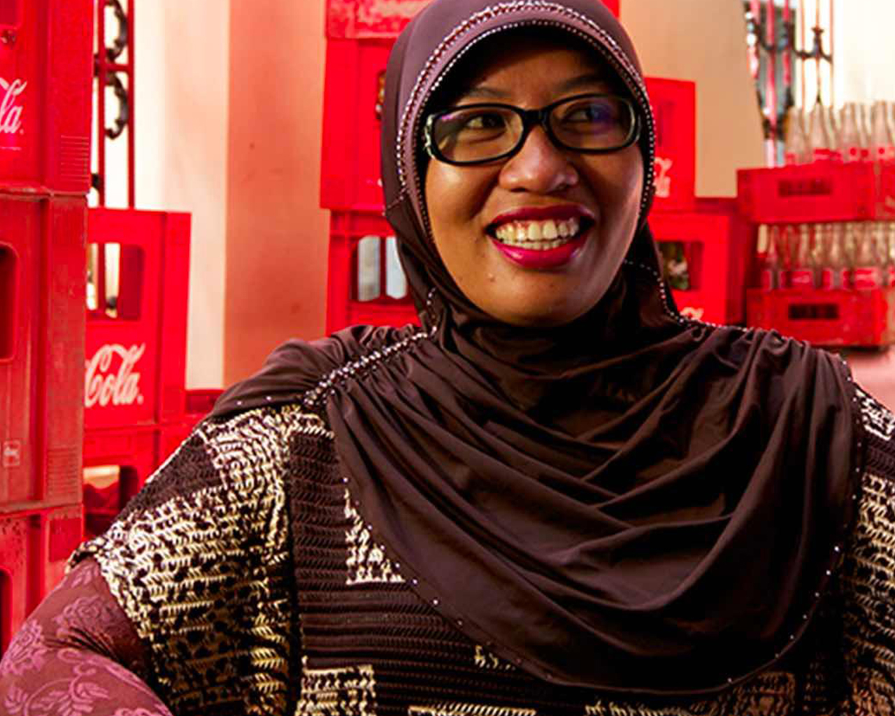 A woman smiling in front of multiple Coca-Cola red boxes