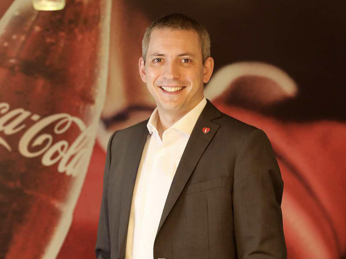 Man in a suit smilling in front of a Coca-Cola banner