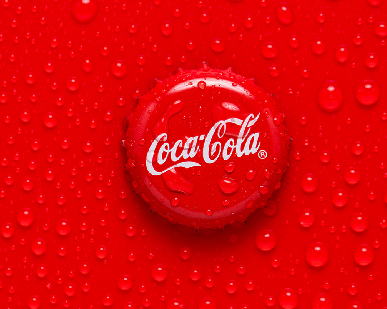 A Coca-Cola cap placed on a red surface with small water droplets