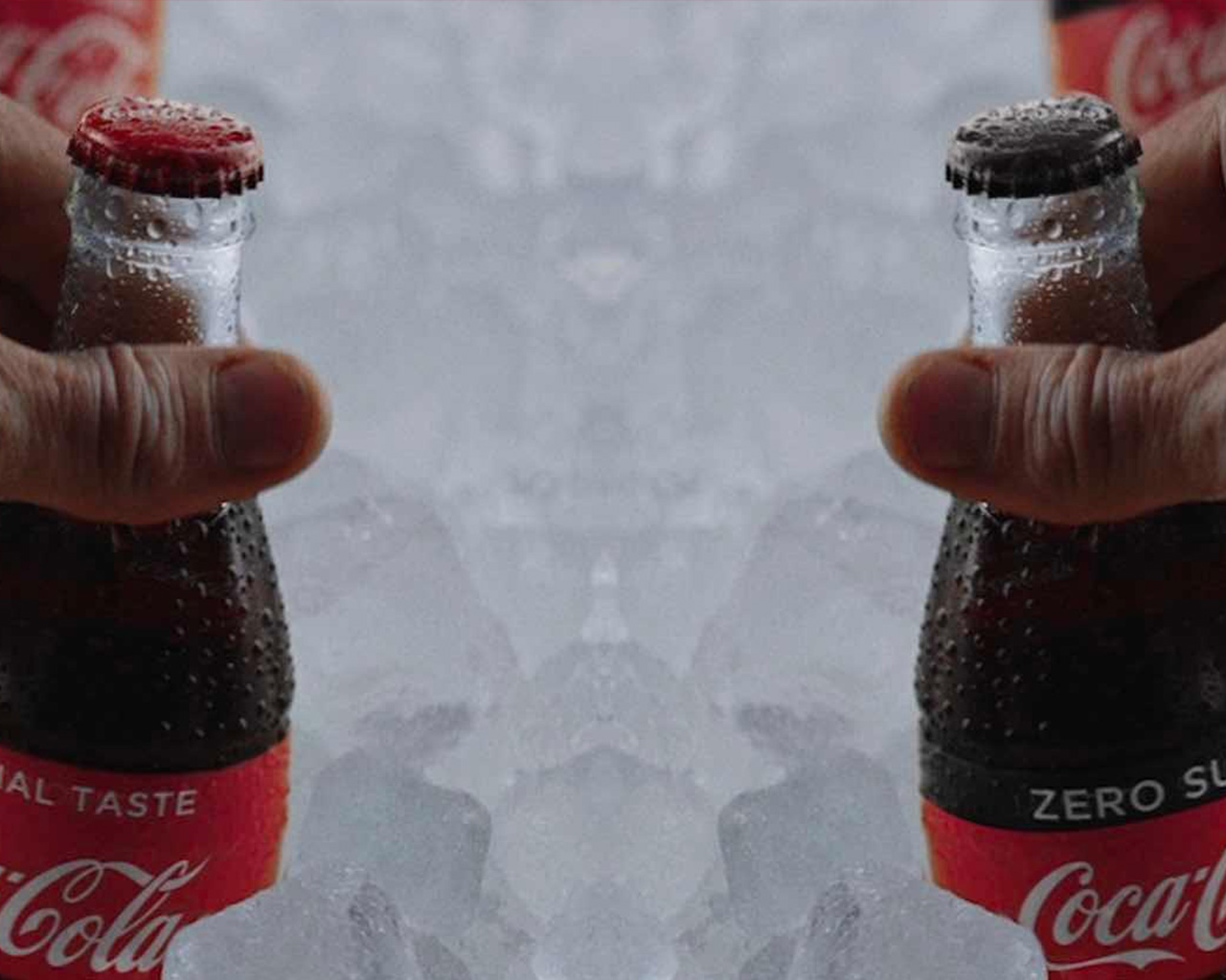  A mirrored image of a hand holding a Coca-Cola bottle inside a large quantity of ice