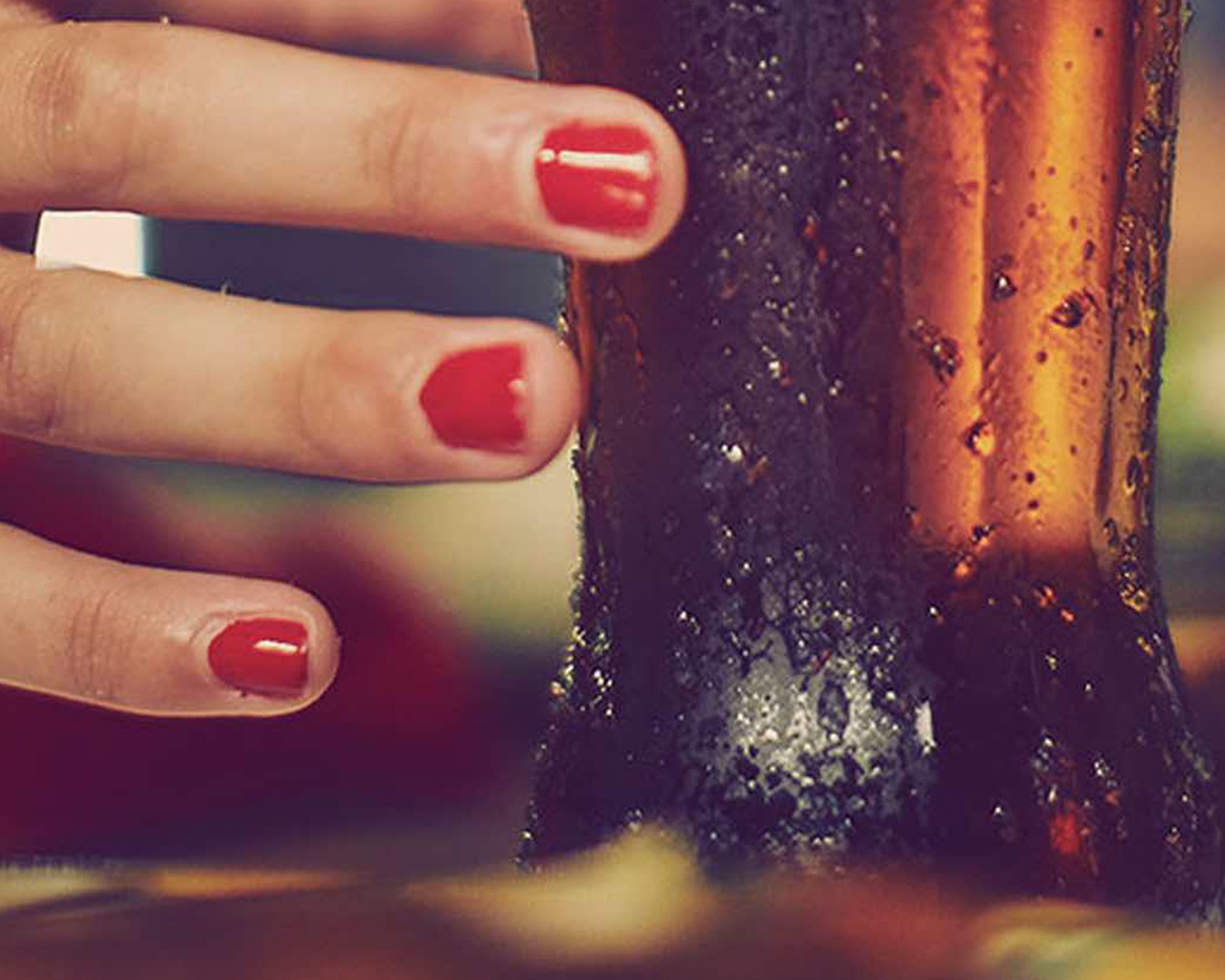 Detail of a hand with red fingernails holding a Coca-Cola bottle