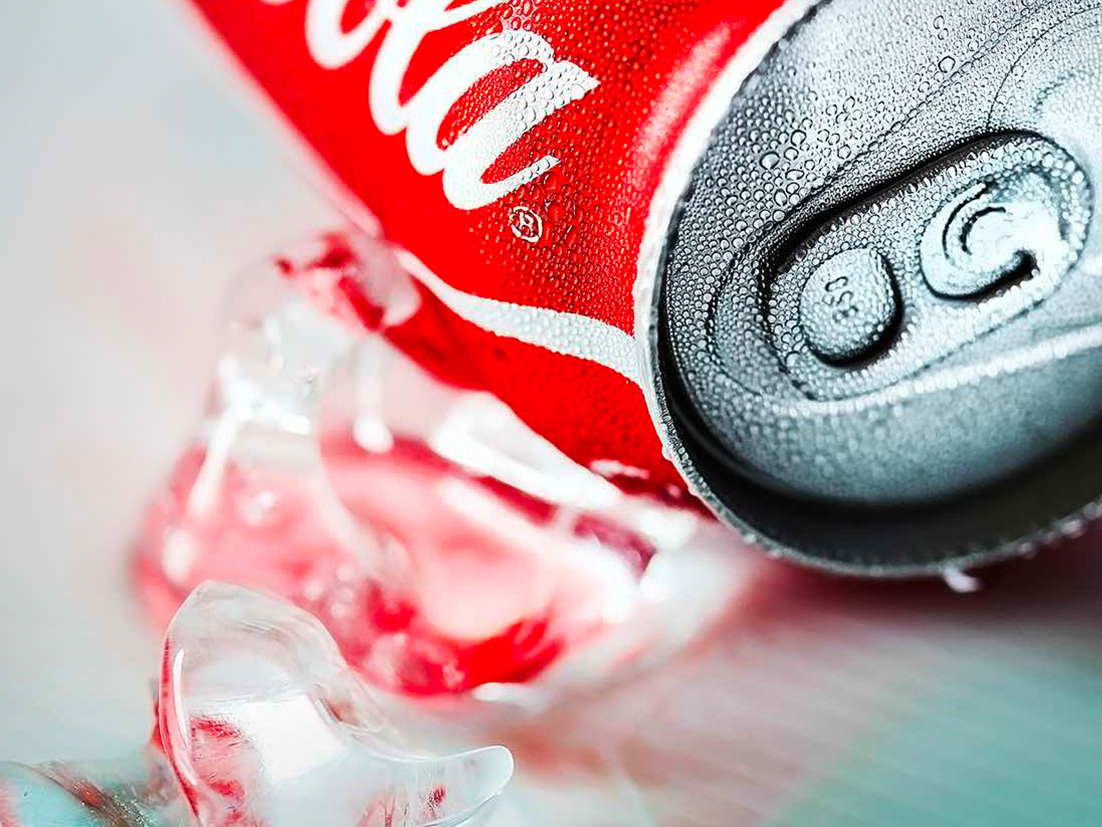 A Coca-Cola can laying next to cubes of ice on a white surface