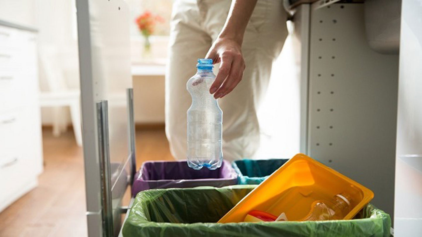 A person putting an empty plastic bottle inside a trash can with a purple plastic bag