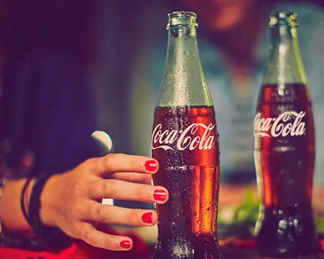 A lady trying to grab a coca-cola bottle, with another coca-cola bottle lying on the side