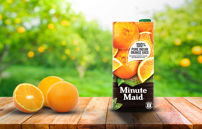 A carton of minute maid orange on a wooden bench in a garden, next to some oranges
