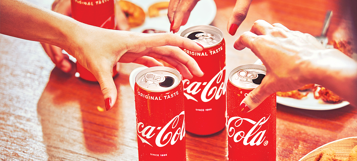 Multiple hands reaching for four open cans of coca-cola.