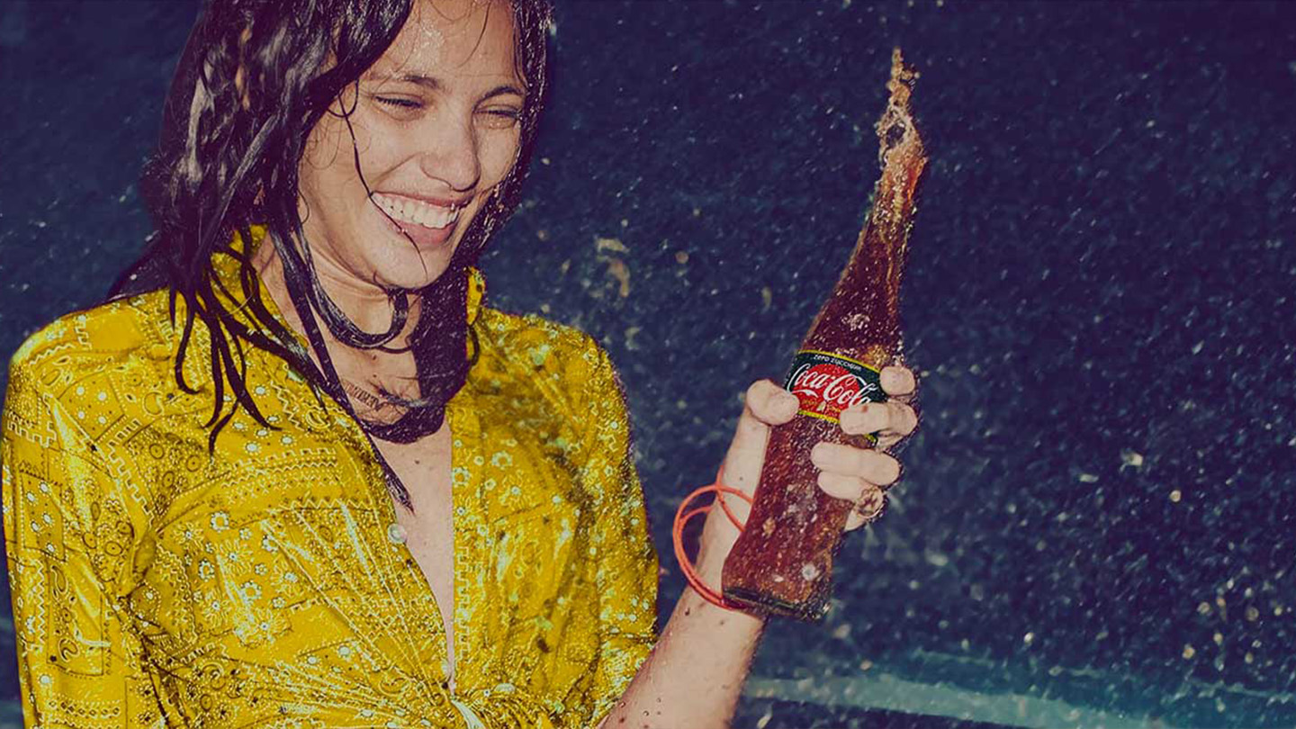 Una ragazza che tiene in mano una bottiglia di Coca-Cola gusto Limone Zero Zuccheri in vetro.