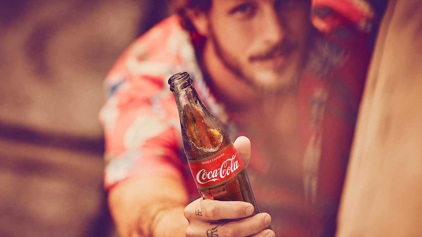 Un ragazzo che tiene in mano una bottiglia di Coca-Cola in vetro.