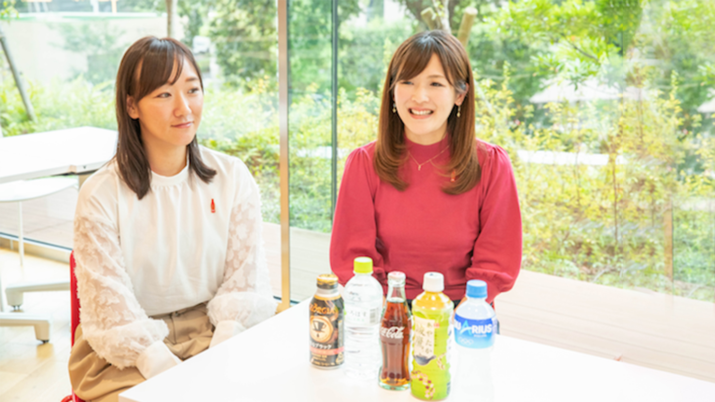 日本コカ･コーラオリンピック専門チーム2人（巻田さんと古長さん）がペットボトル・ドリンクを前に座っている写真