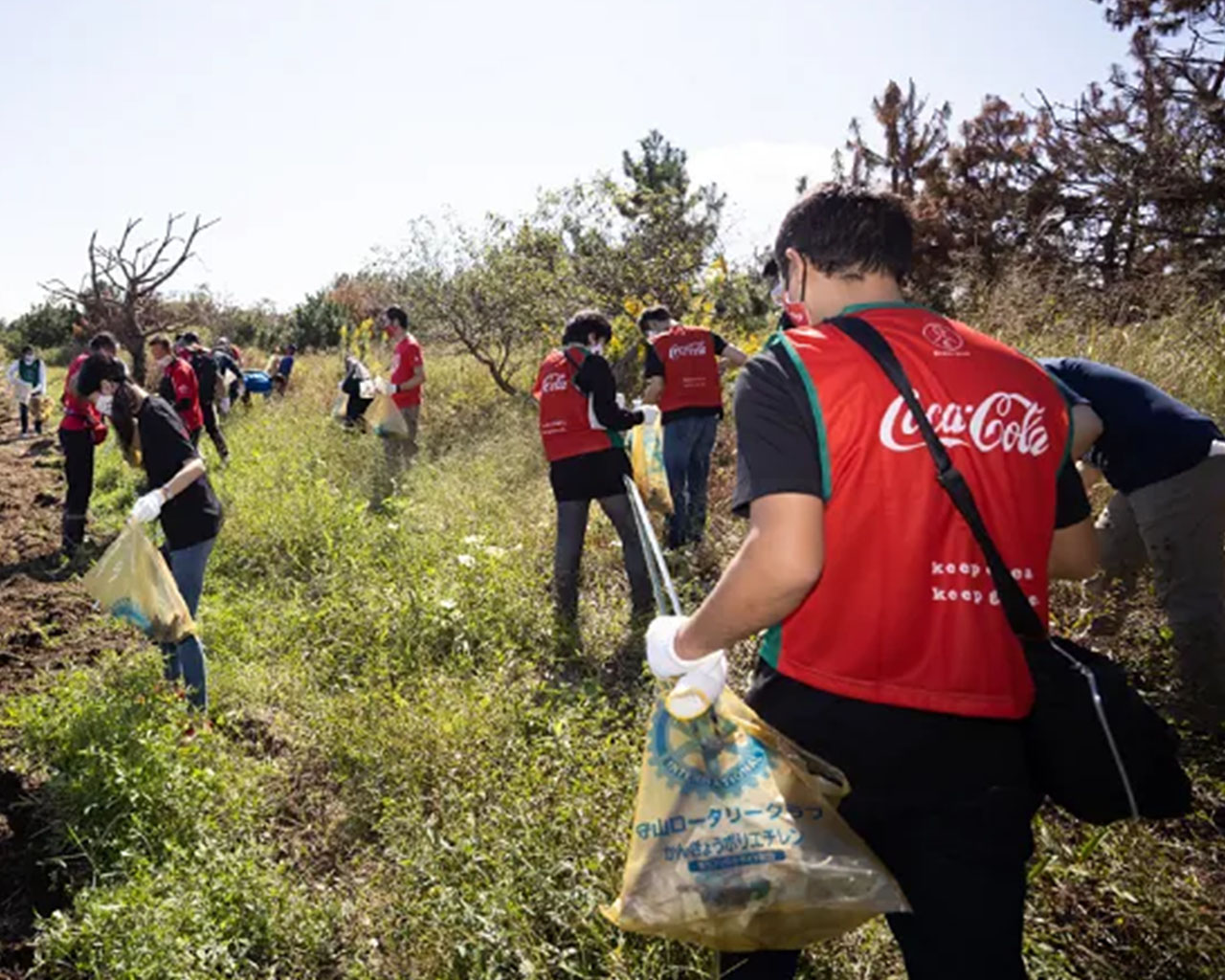 コカ・コーラの赤いベストを着用して清掃ボランティア活動をする人々