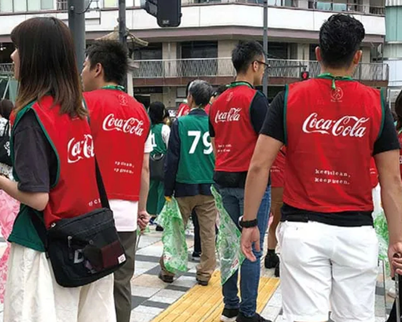 コカ・コーラの赤いベストを着用し清掃活動に参加する人々