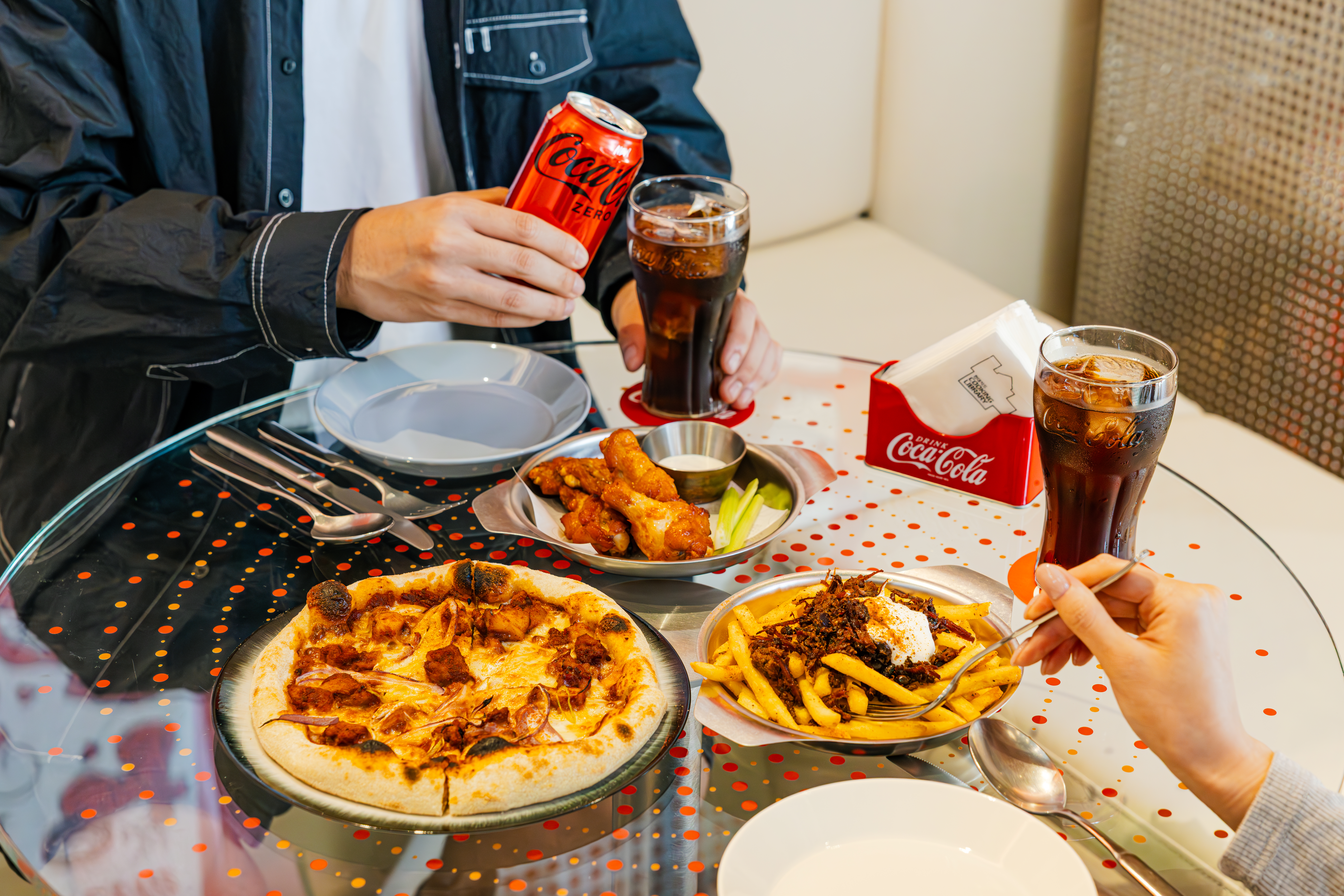 한정판 코카-콜라 콤보 메뉴 4종, 치폴레 치킨 피자와 비프 베이컨 감자튀김, 그리고 버팔로윙과 함께 코카-콜라 제로를 즐기는 사진.