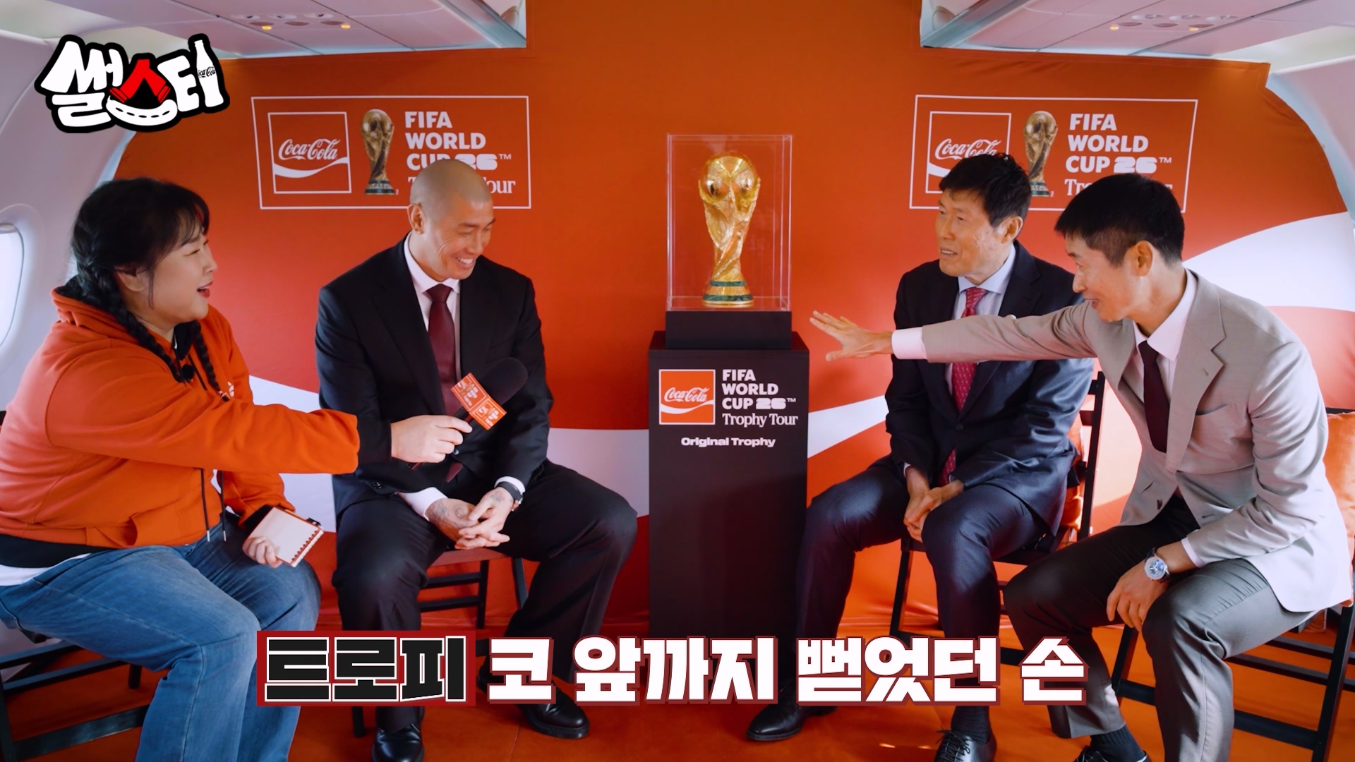 MC 콕키퍼 김민경이 코카-콜라 전용기 내부에서 FIFA 월드컵 트로피를 중앙에 두고 한국 축구 레전드들과 인터뷰를 진행중인 장면