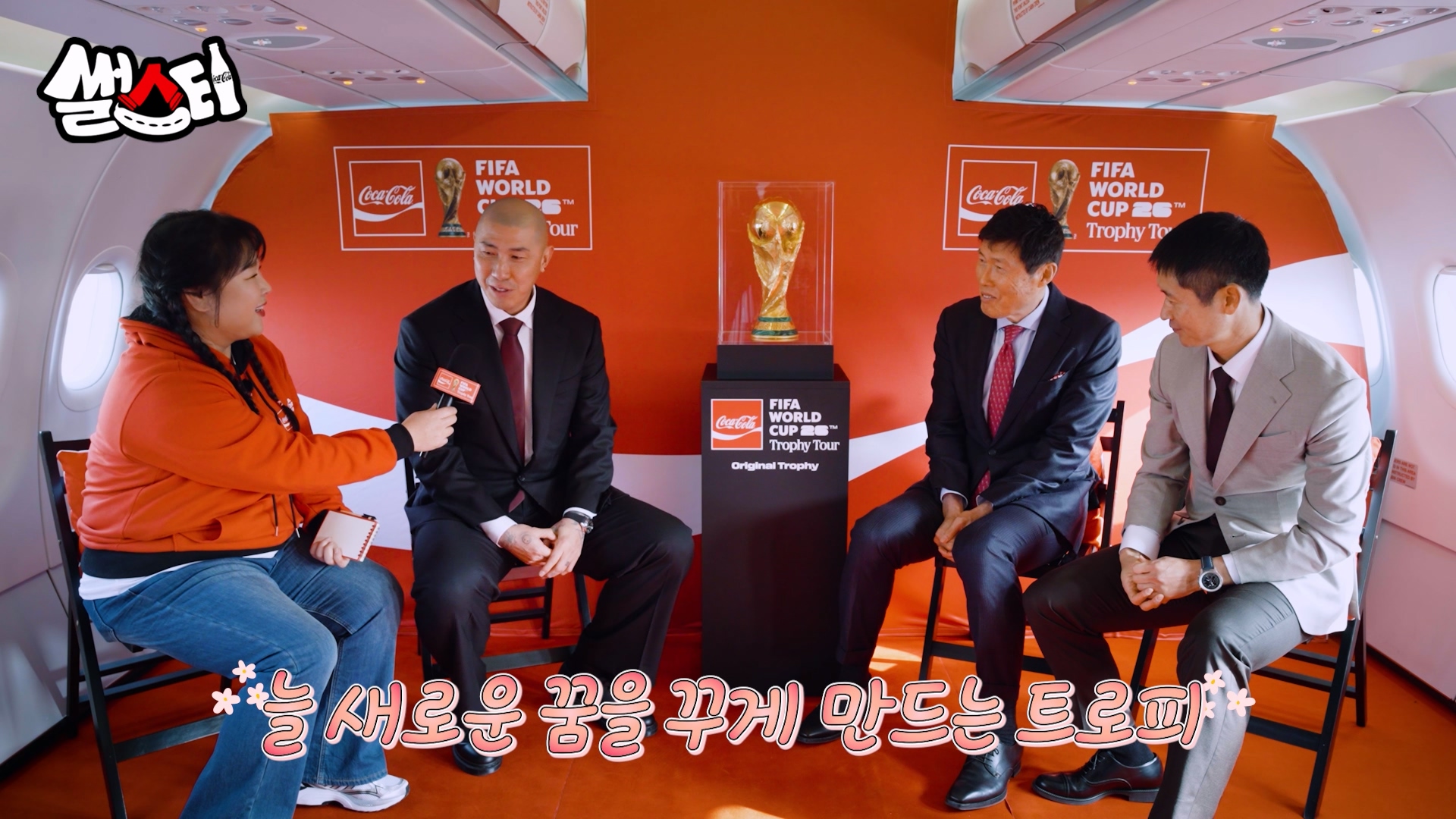 MC 콕키퍼 김민경이 코카-콜라 전용기 내부에서 FIFA 월드컵 트로피를 중앙에 두고 한국 축구 레전드들과 인터뷰를 진행중인 장면