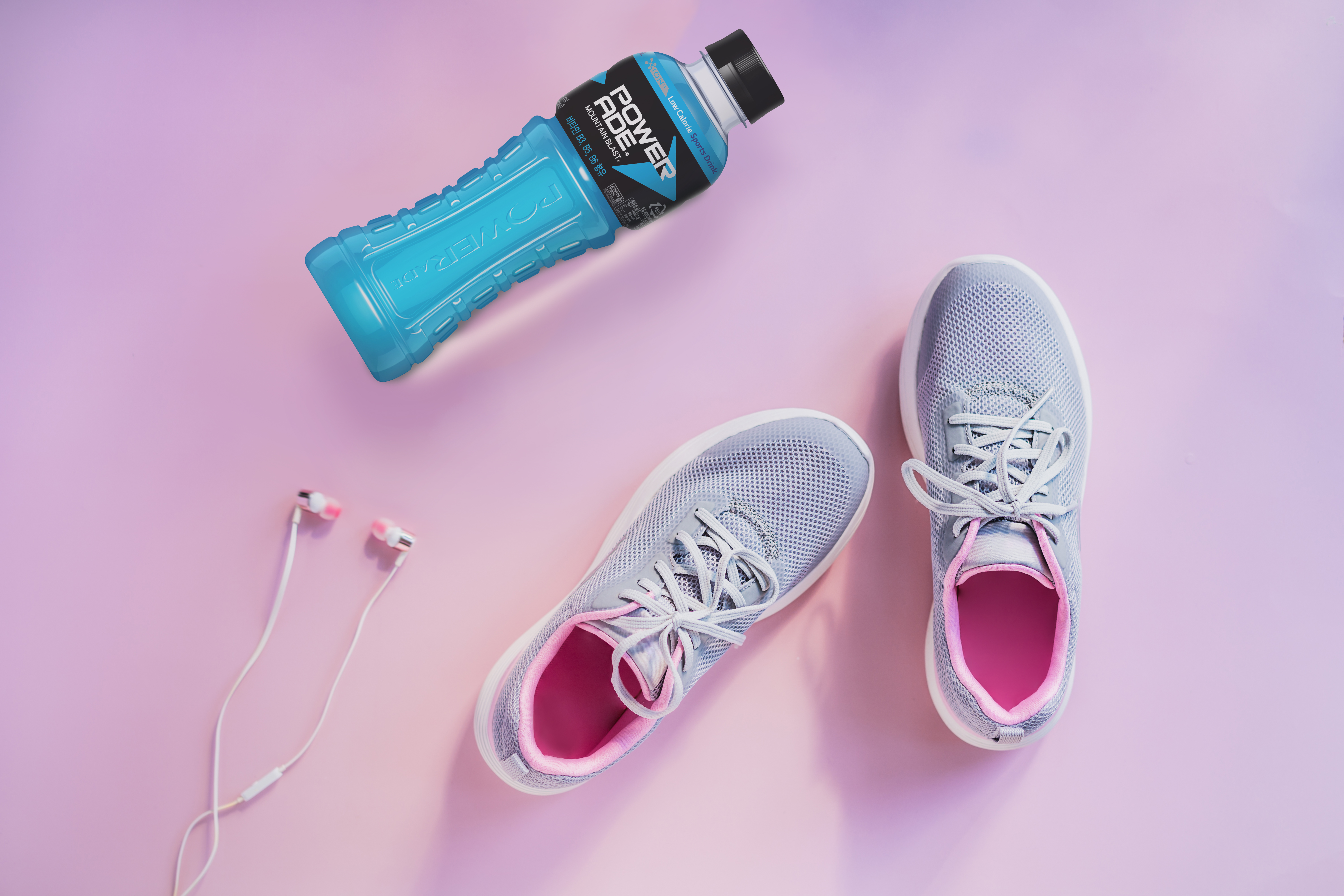 Top view sneakers, earphones and glass water bottle on a pink background. Set for running and sports activities. Healthy and active lifestyle. Online workout. Flat lay. Copy space