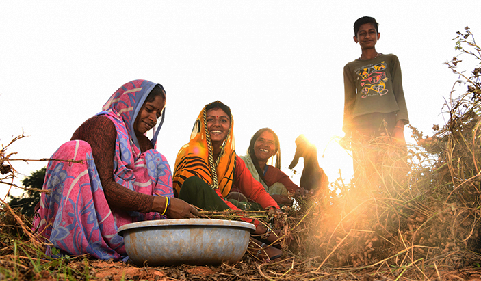 Women and children sat in the grass with a large cooking pot.