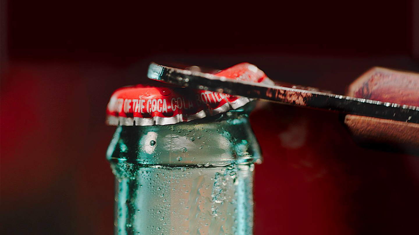 coca-cola stikla pudelē ar sarkanu korķi un pudeļu atveramo
