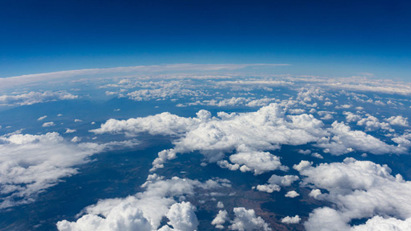 Peisaj cu cer albastru și norișori albi, lac în prim-plan, o zonă cu iarbă și munți în depărtare