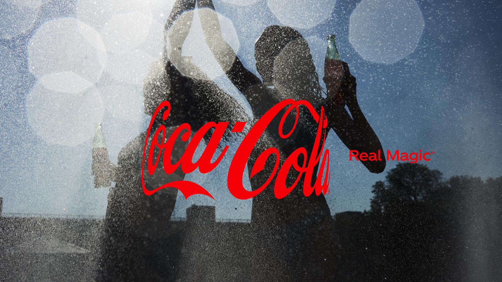 coca-cola baner sa crvenim logoom u fokusu i dvije đevojke plešu u pozadini