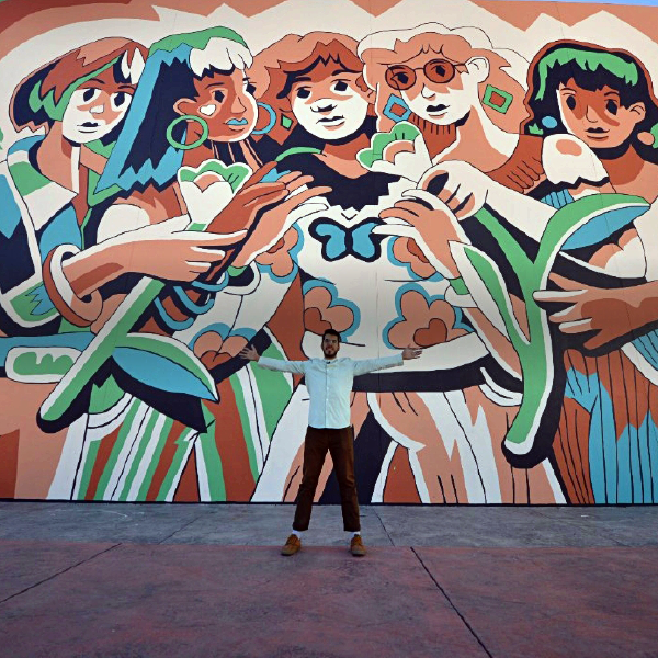 Hombre posa con los brazos abiertos, frente a un mural