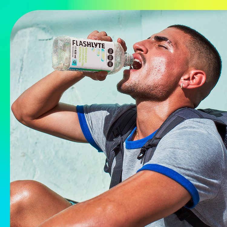Un hombre activo bebiendo entusiasmadamente una botella de Flashlyte, una bebida deportiva con electrolitos, destacando su refrescante efecto mientras está al aire libre y llevando una mochila.​