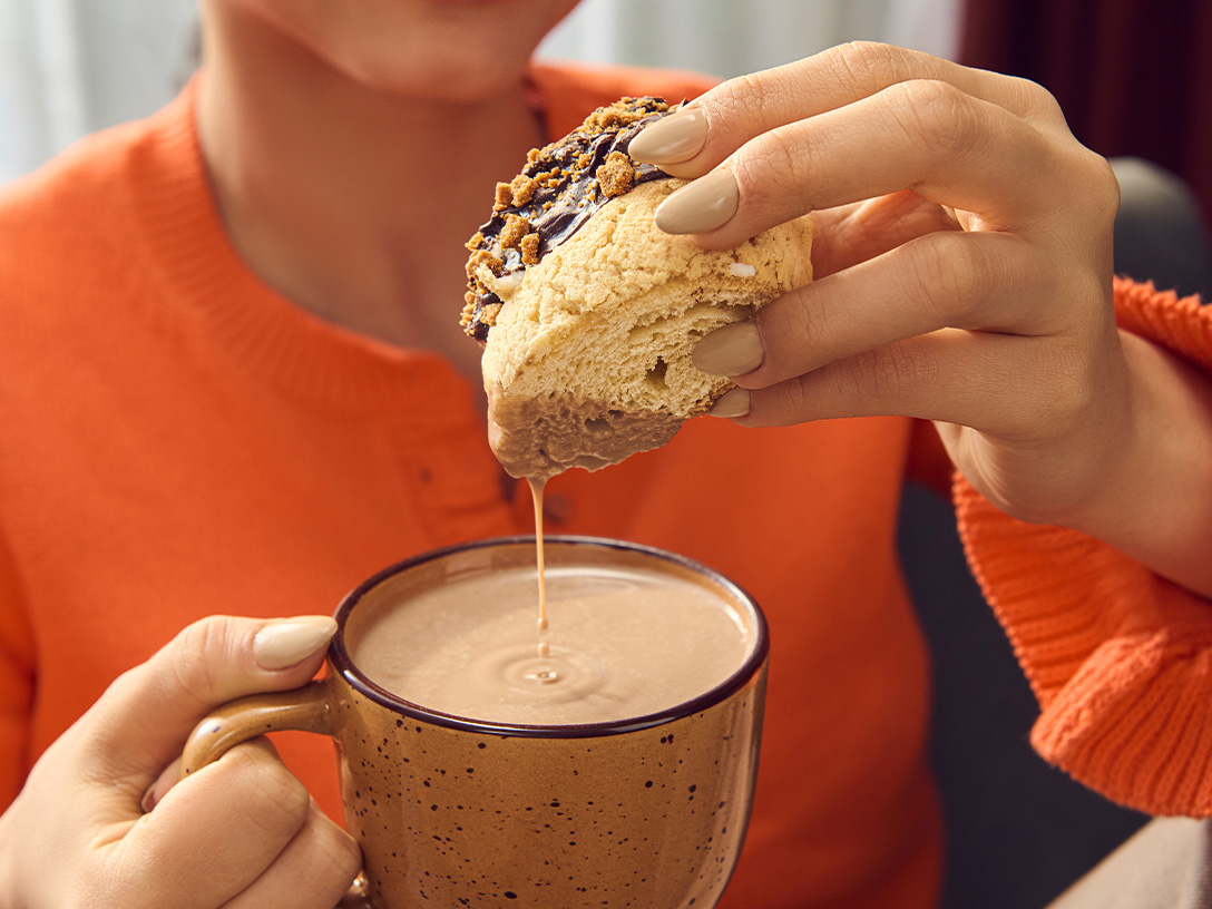 Una persona sumerge un pan dulce en una taza de chocolate mexicano, con un hilo de chocolate goteando.