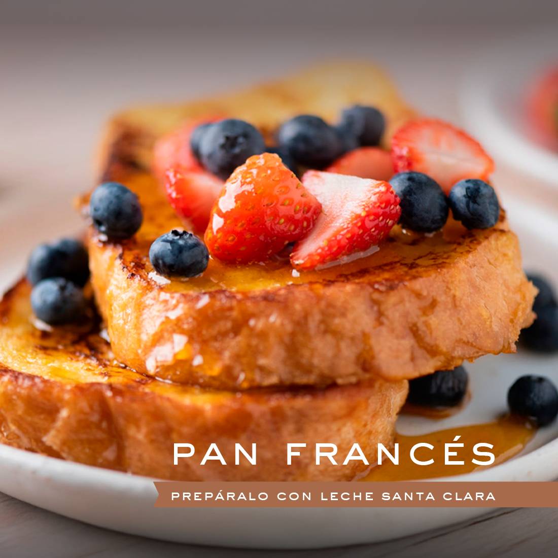 Dos rebanadas de tostadas francesas doradas apiladas en un plato blanco, cubiertas con arándanos frescos y fresas en rodajas, y bañadas en jarabe.