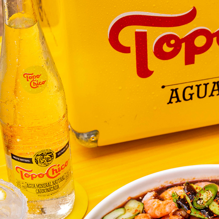 Botella de Topo Chico agua, con plato de comida y hielera Topo Chico.